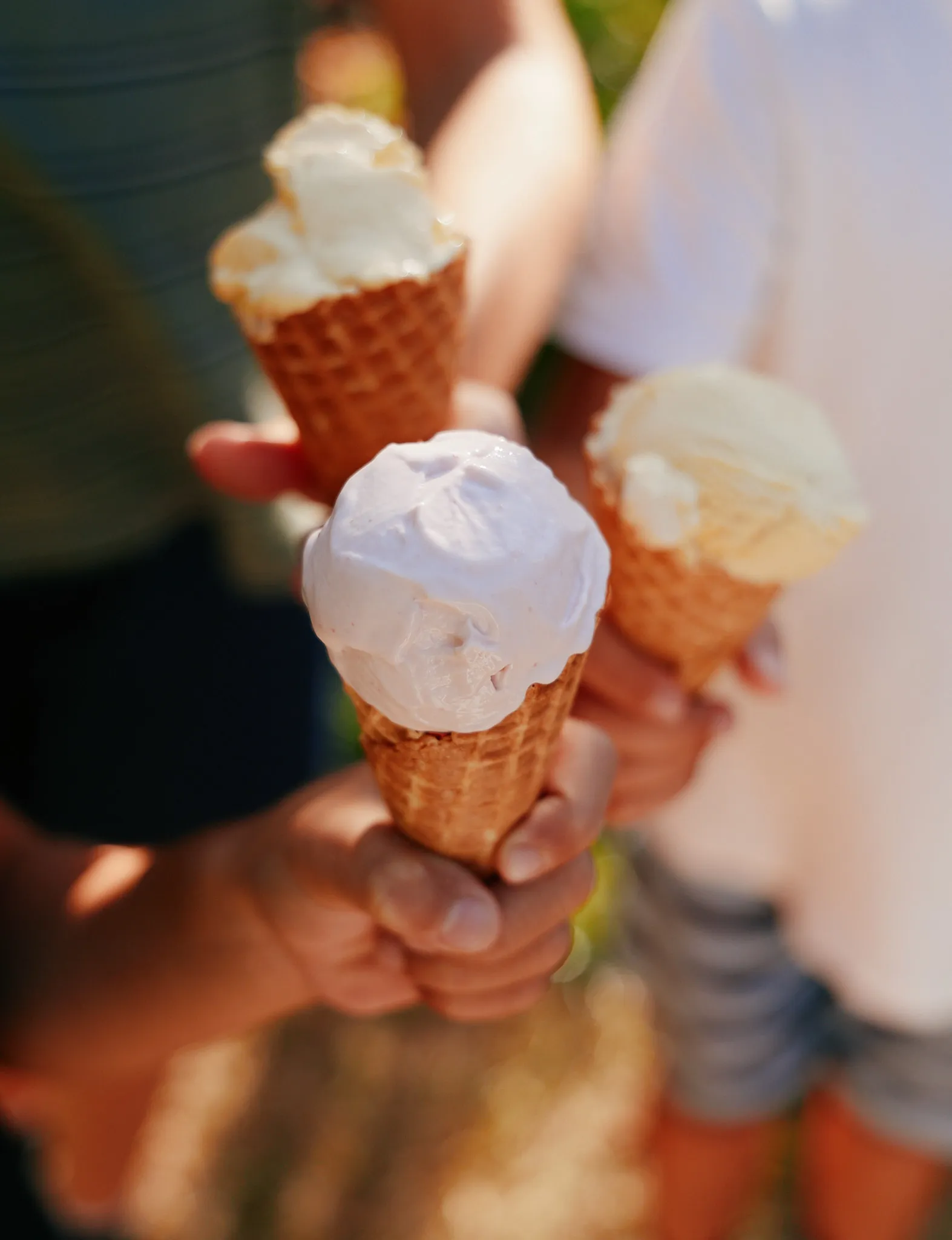 Three children holding homemade ice cream cones out towards the camera in the sunshine.